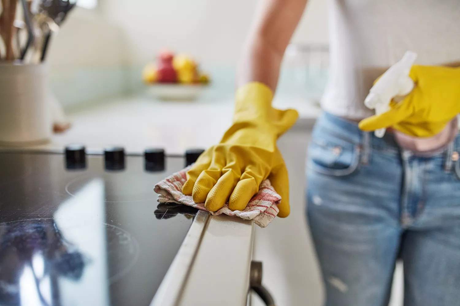 Woman wiping stovetop with cloth while wearing gloves